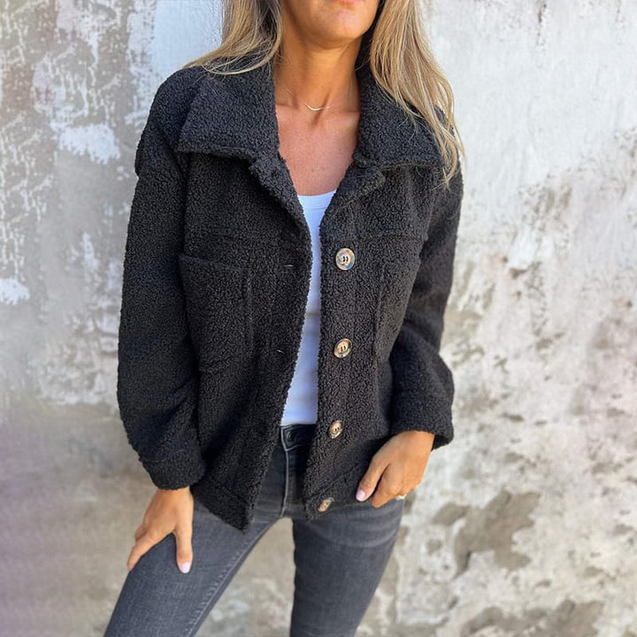 Schwarze Teddyjacke für Damen mit Knopfleiste, Umlegekragen und zwei Brusttaschen aus flauschigem Material.