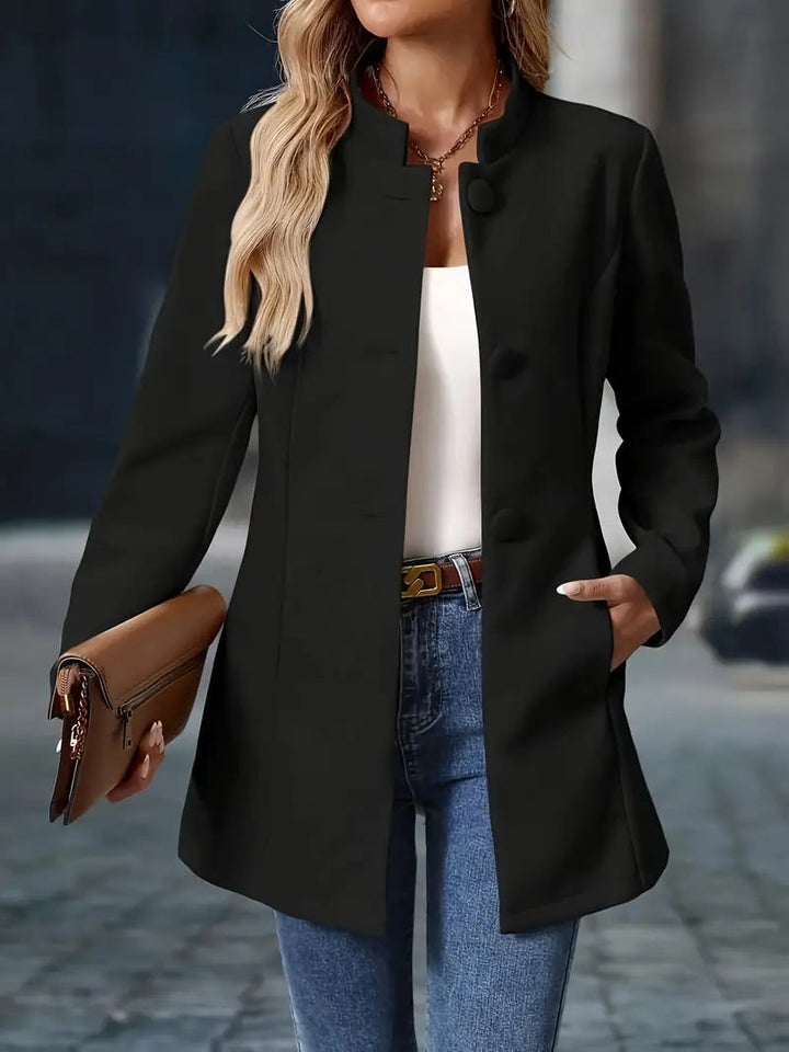 Taillierter schwarzer Damenmantel mit Stehkragen, Knopfleiste und Seitentaschen, kombiniert mit Jeans und Clutch.