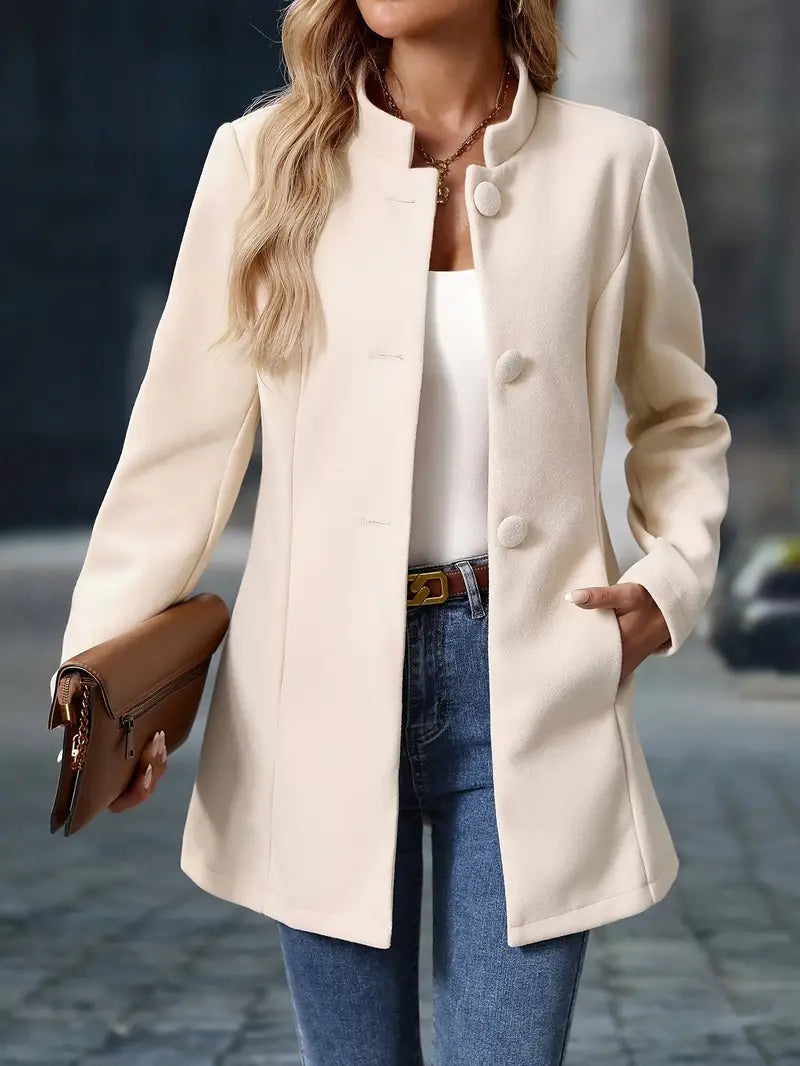 Beiger Damenmantel mit Stehkragen, Knopfleiste und tailliertem Schnitt, kombiniert mit Jeans und brauner Clutch.