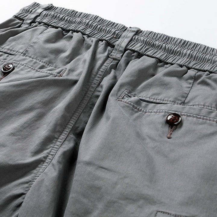 Graue Herren-Cargoshorts mit elastischem Bund, Kordelzug und zwei geknöpften Gesäßtaschen aus robustem Baumwollstoff.