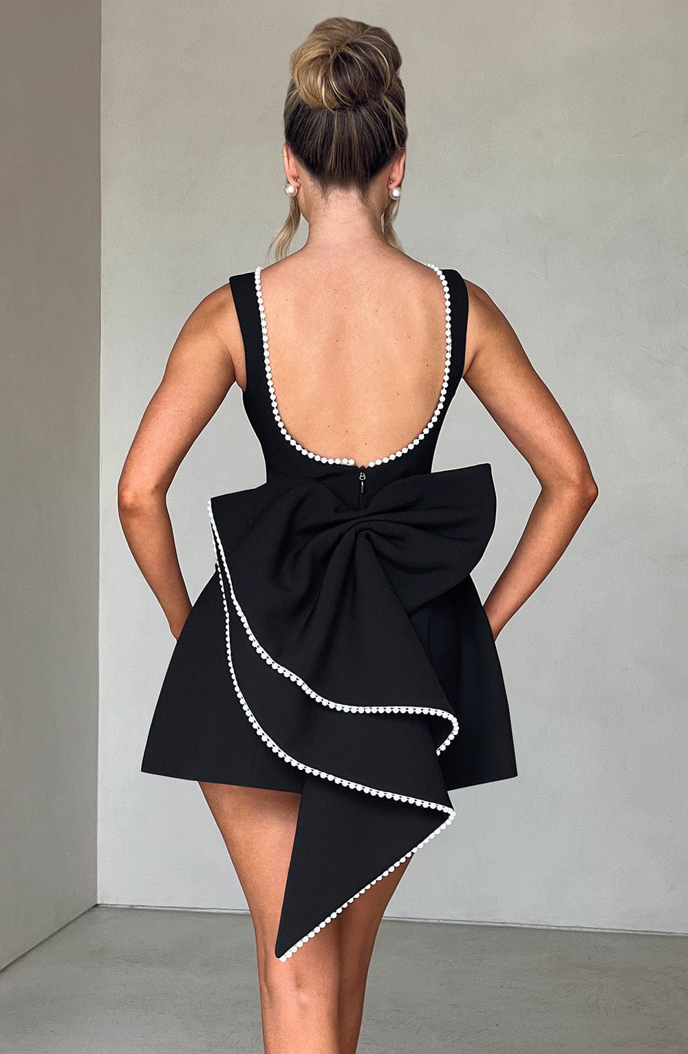 Schwarzes Leonie Minikleid mit tiefem Rückenausschnitt und großer Schleife mit Perlenbesatz.