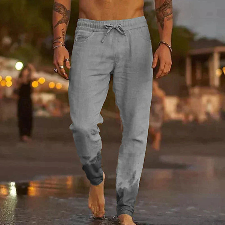 Graue Herren-Leinenhose mit elastischem Kordelzugbund und lockerem Schnitt am Strand.