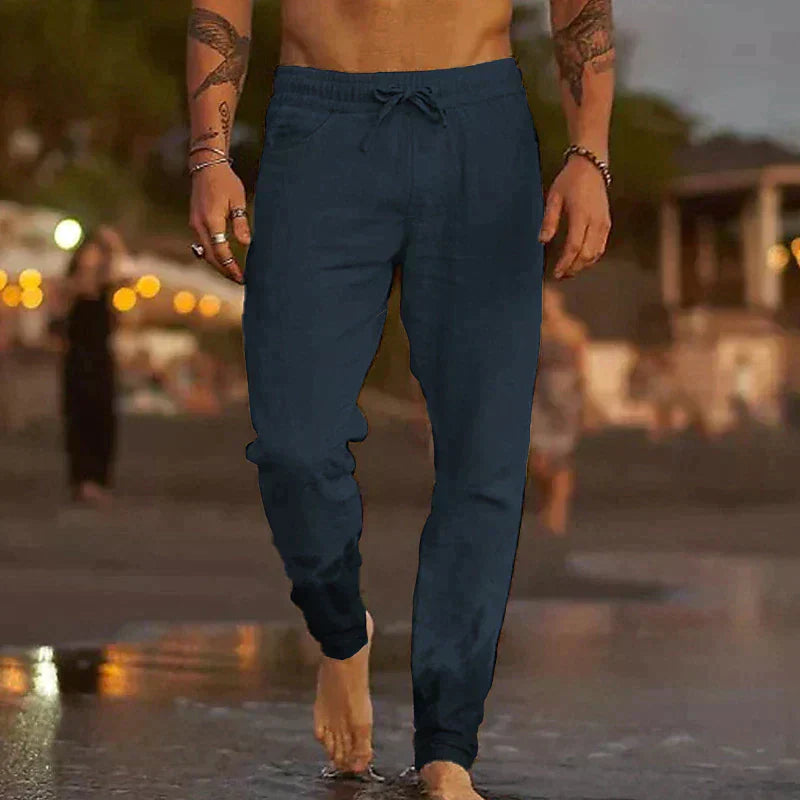 Dunkelblaue Herren-Leinenhose mit elastischem Kordelzugbund in lockerem Schnitt am Strand.