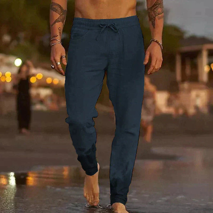 Dunkelblaue Herren-Leinenhose mit elastischem Kordelzugbund in lockerem Schnitt am Strand.