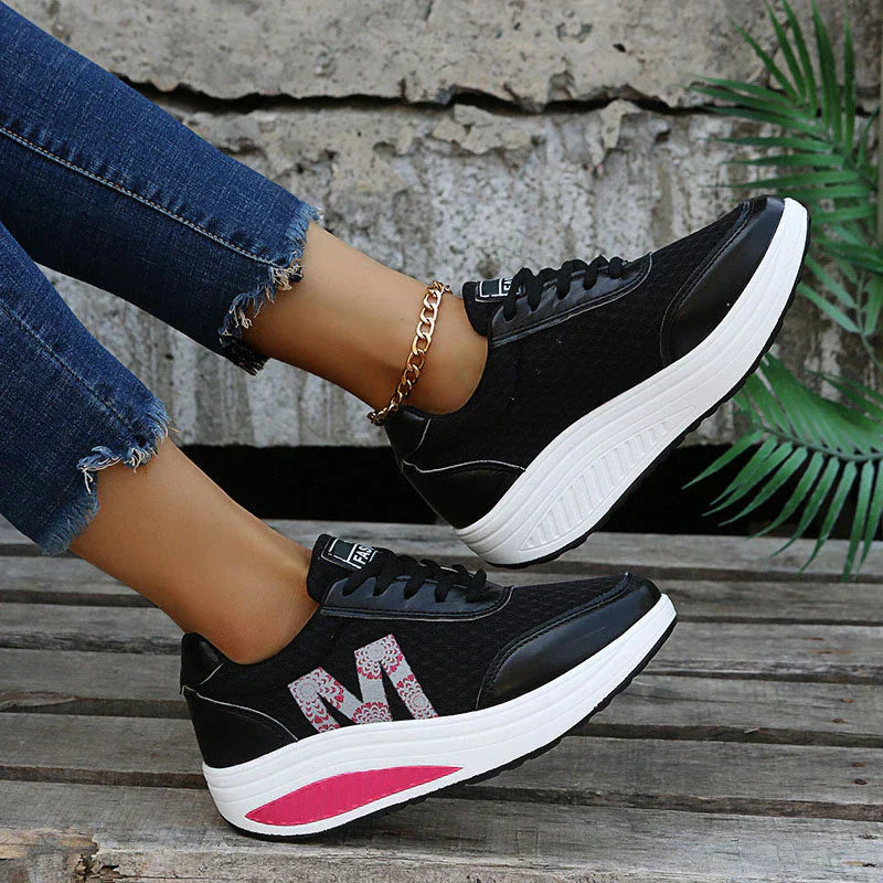 Schwarzer Damen-Plateau-Sneaker aus Mesh mit floralem M-Logo und weißer Keilsohle mit pinkem Akzent.