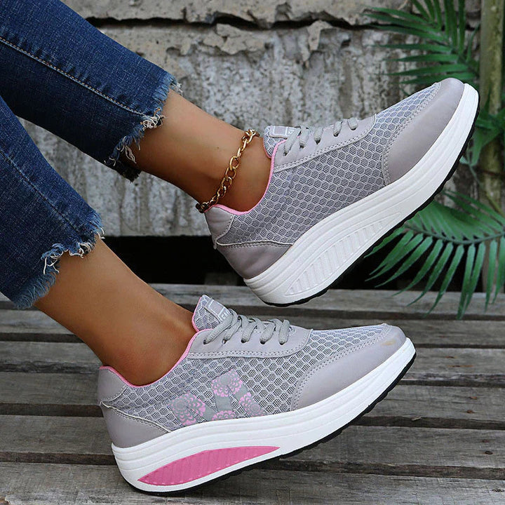 Graue Livia Plateau-Sneaker aus Mesh mit rosa Blütenprint, Schnürung und weißer Keilsohle an einem Fuß getragen.