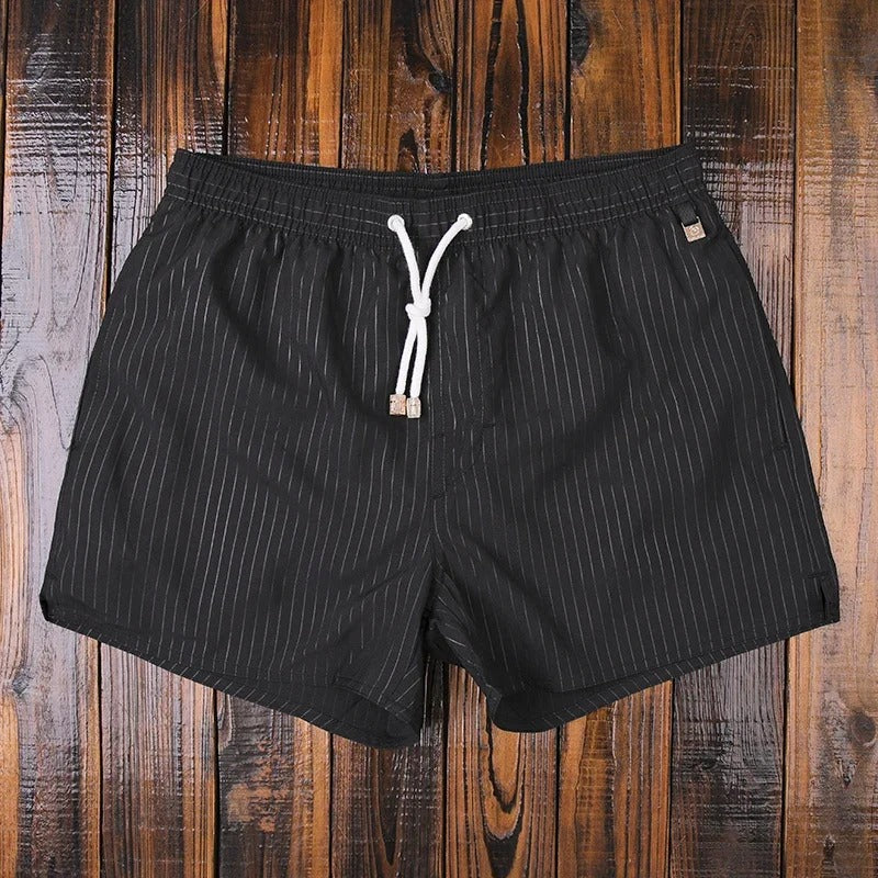 Schwarze Lukas Badeshorts für Herren mit feinen vertikalen Streifen, elastischem Bund und weißem Kordelzug.