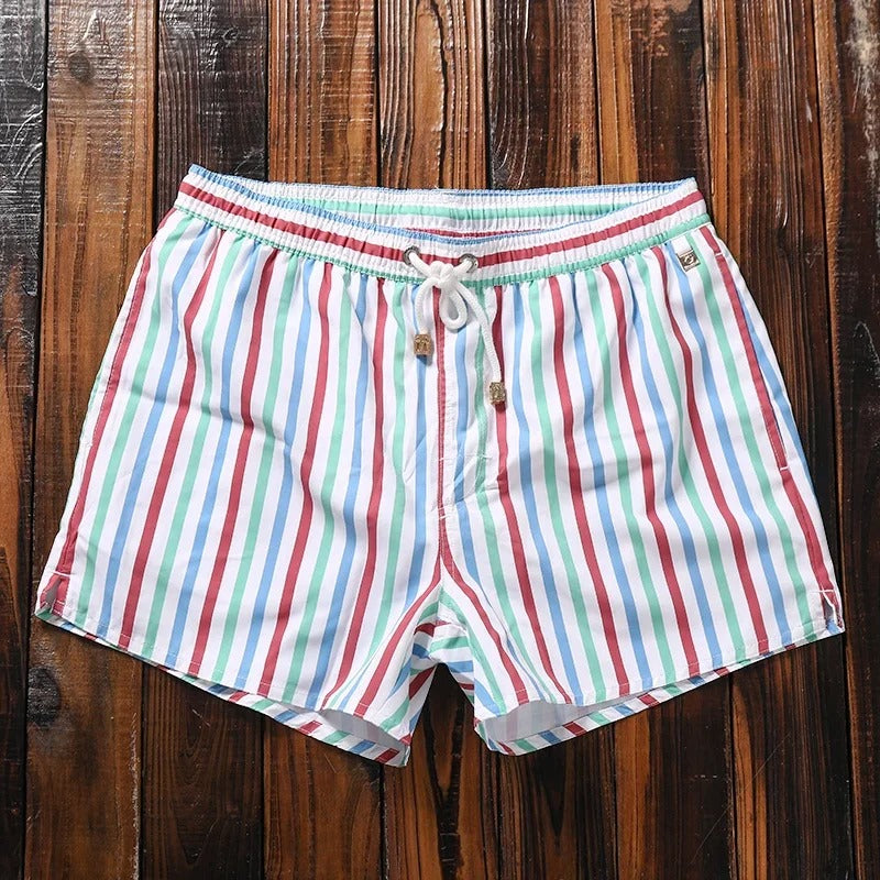 Lukas Herren-Badeshorts mit buntem Streifenmuster, elastischem Bund und weißem Kordelzug auf rustikalem Holzhintergrund.