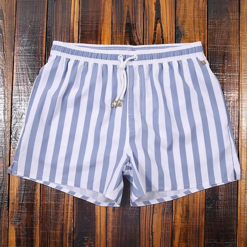 Lukas Herren-Badeshorts mit blau-weißem Streifenmuster, elastischem Bund und weißem Kordelzug auf Holzuntergrund.