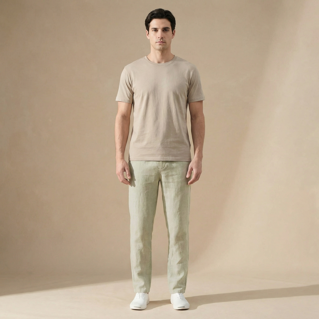Mann in hellgrüner Leinenhose mit geradem Schnitt und beigem T-Shirt vor neutralem Hintergrund.