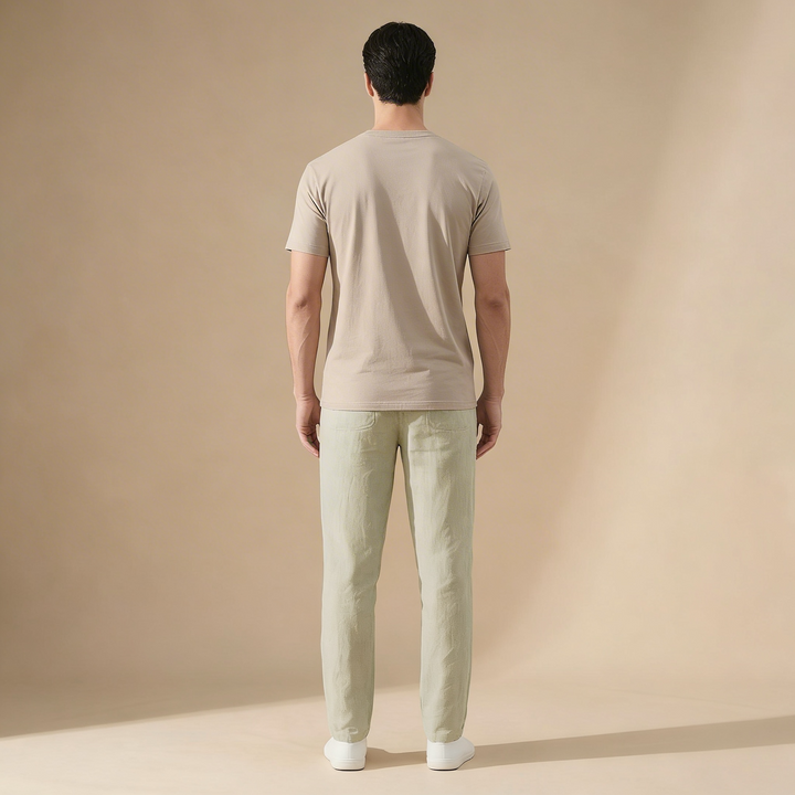 Rückenansicht einer hellgrünen Herren-Sommerhose in Leinen-Optik mit geradem Schnitt und beigem T-Shirt auf beigem Grund.