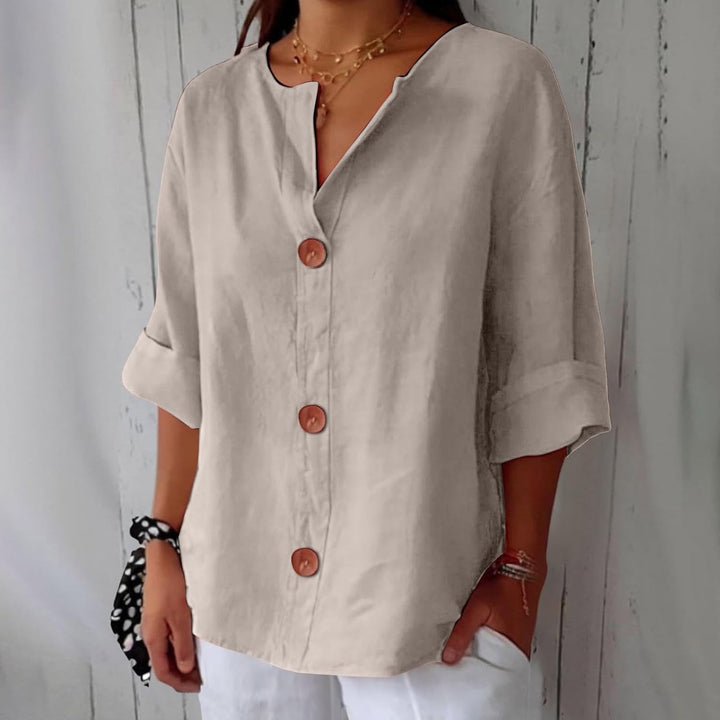 Beige Leinenbluse mit V-Ausschnitt, 3/4-Ärmeln und großen braunen Knöpfen in lockerer Passform.