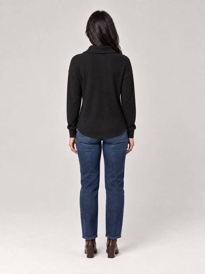 Schwarzer Damen-Troyer in Waffelstrick mit Stehkragen und lockerer Passform, kombiniert mit blauer Jeans.