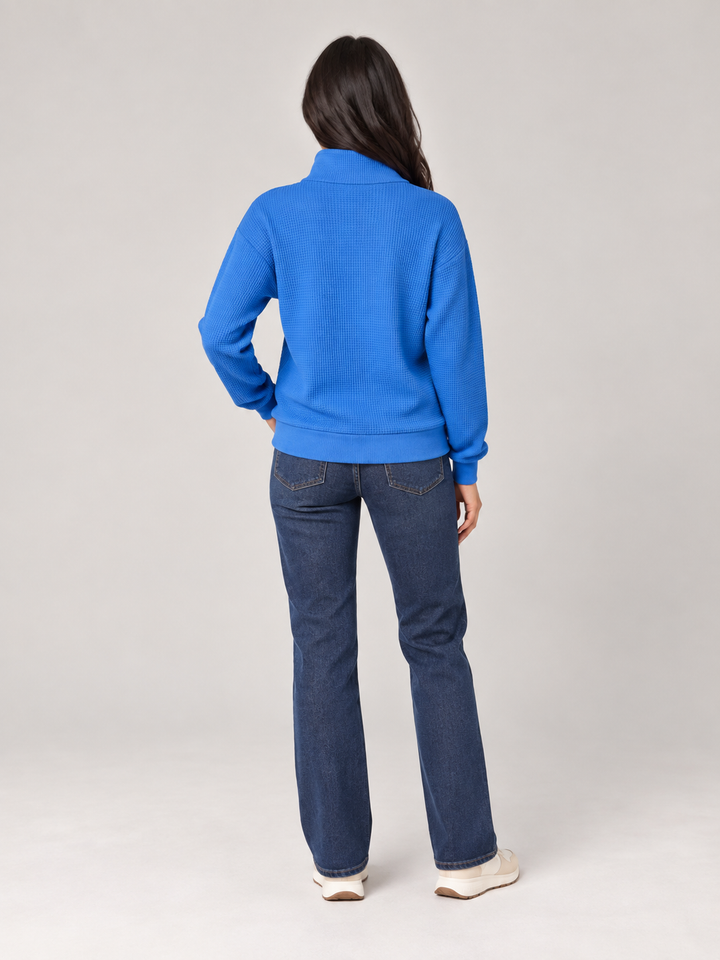 Blauer Damen-Troyer in Waffelstrick mit Stehkragen und Reißverschluss in lockerer Passform kombiniert mit Jeans.