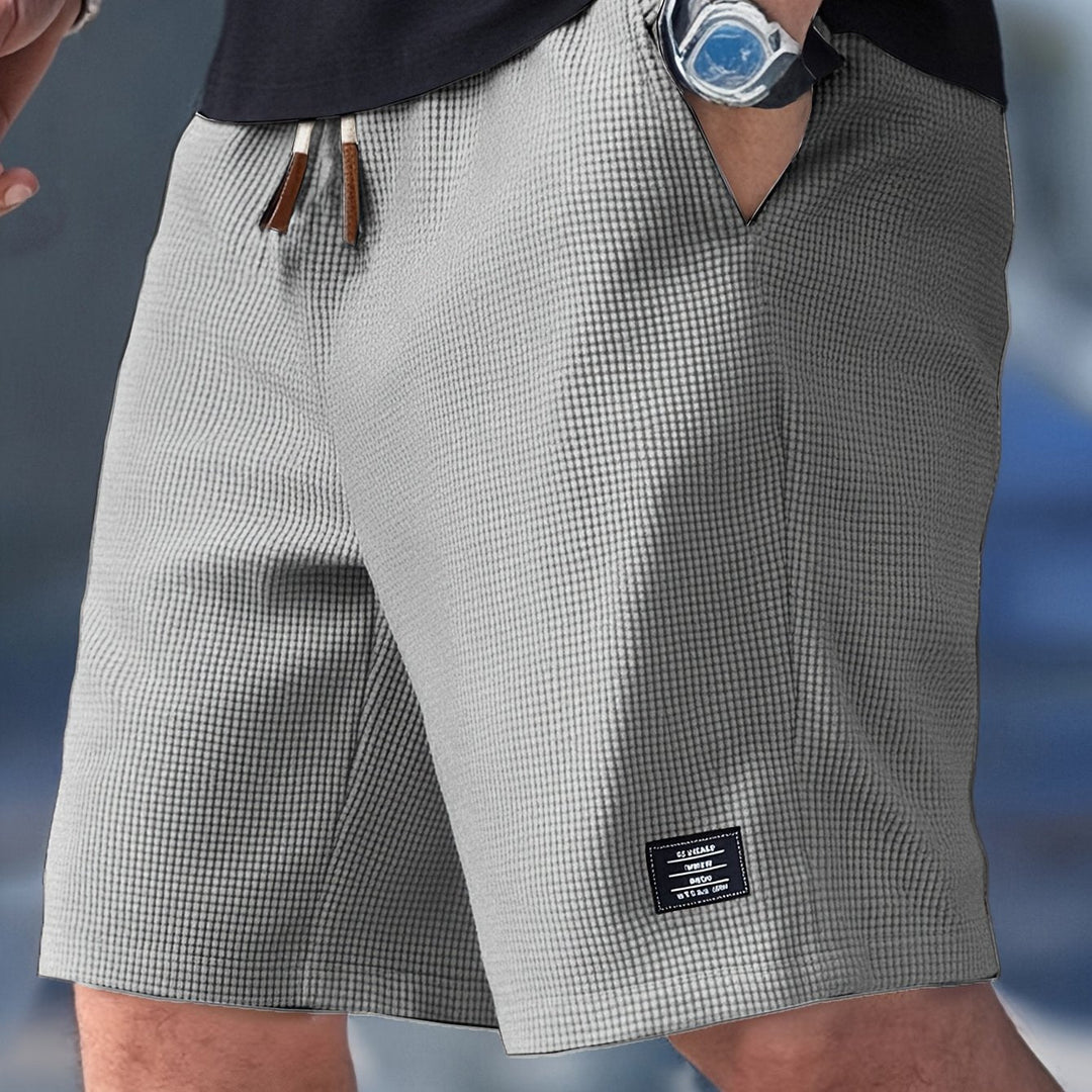 Graue Herrenshorts in Waffelstruktur mit elastischem Bund, Kordelzug und kleinem Logo-Patch am Bein.