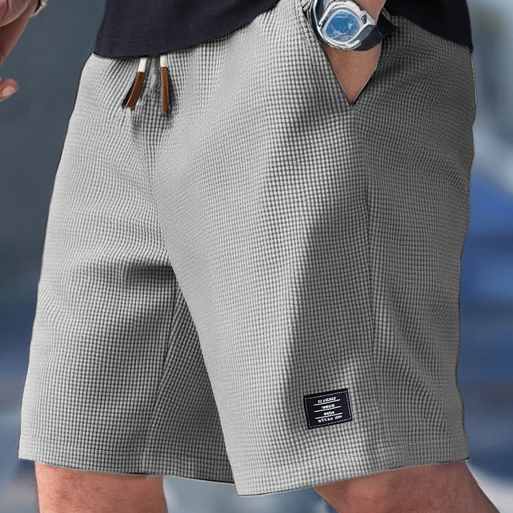 Graue Herrenshorts in Waffelstruktur mit elastischem Bund, Kordelzug und kleinem Logo-Patch am Bein.