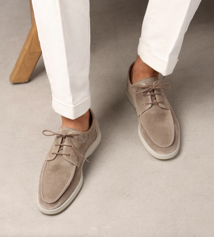 Beigefarbene Marco Herren-Schnürschuhe aus weichem Wildleder mit heller Sohle und klassischer Schnürung zu weißer Hose.