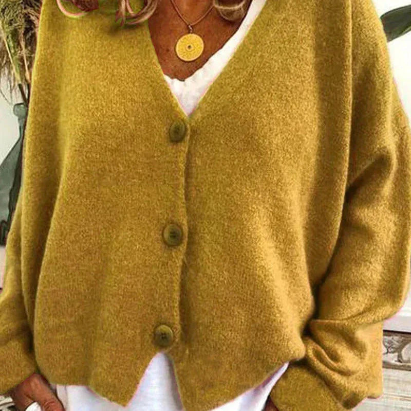 Senfgelbe Damen-Strickjacke Noemi mit V-Ausschnitt, Knopfleiste und weicher Textur über einem weißen Oberteil.
