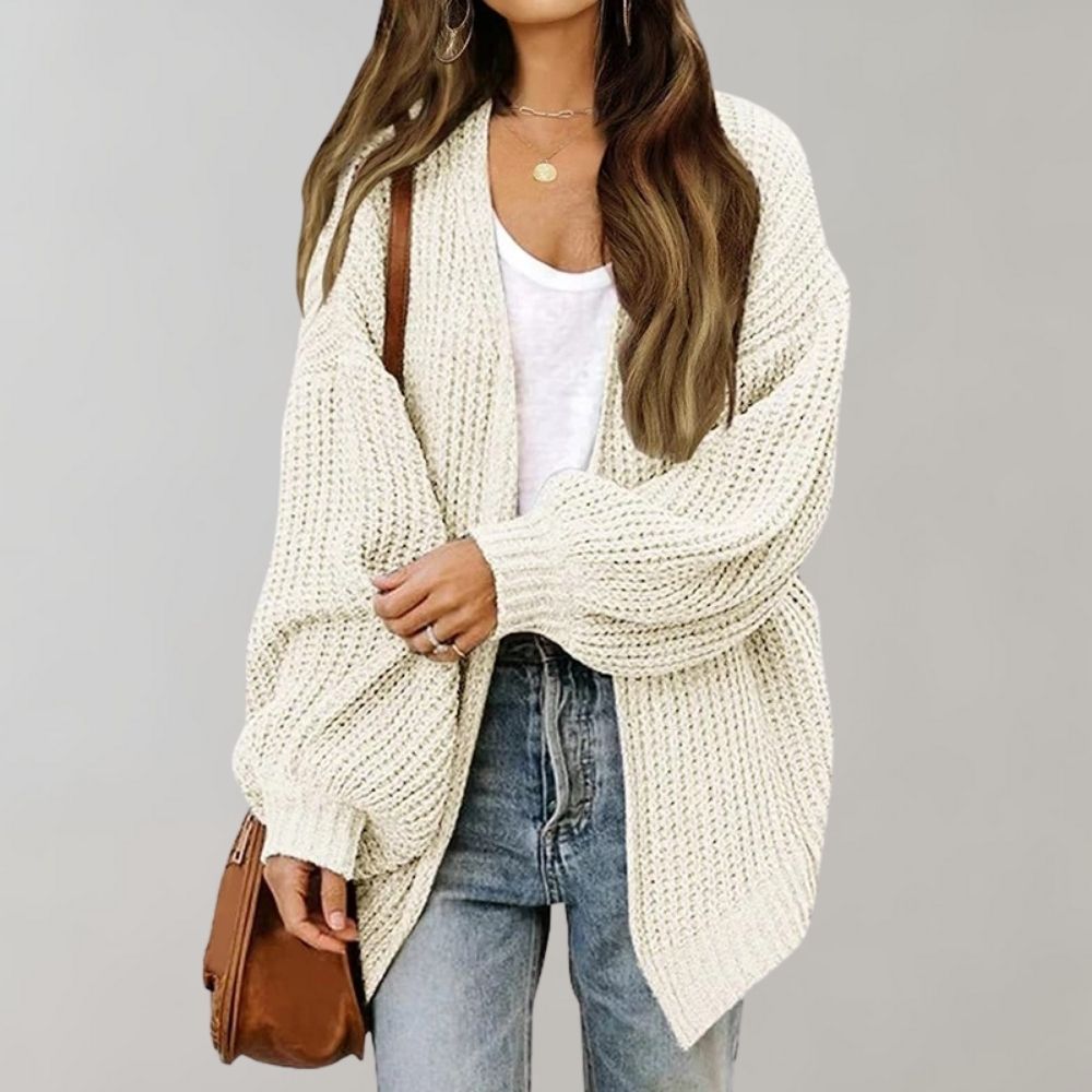 Cremeweiße, grob gestrickte Oversized-Strickjacke mit offener Vorderseite und weiten Ärmeln kombiniert mit Jeans.