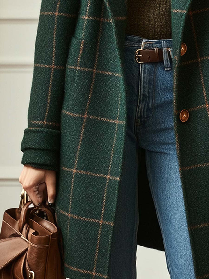 Dunkelgrüner Wollmantel mit braunem Karomuster, Reverskragen und Knopfleiste, kombiniert mit blauer Jeans und brauner Tasche.