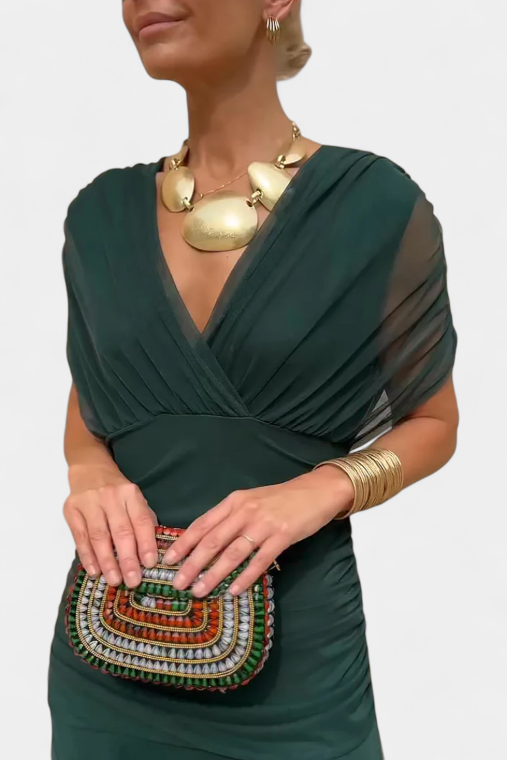 Dunkelgrünes Melina Maxikleid mit V-Ausschnitt, drapiertem Oberteil und geraffter Taille, kombiniert mit goldenem Schmuck.