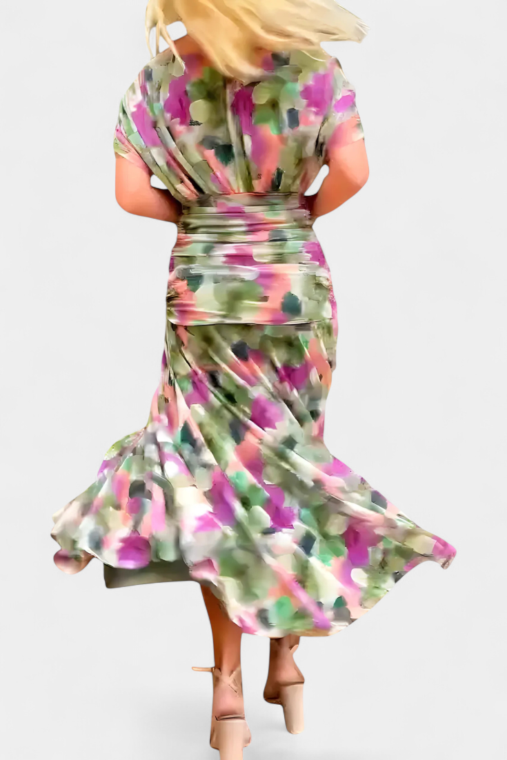 Blondes Model in einem fließenden, bunten Maxikleid mit geraffter Taille und drapiertem Oberteil auf weißem Hintergrund.