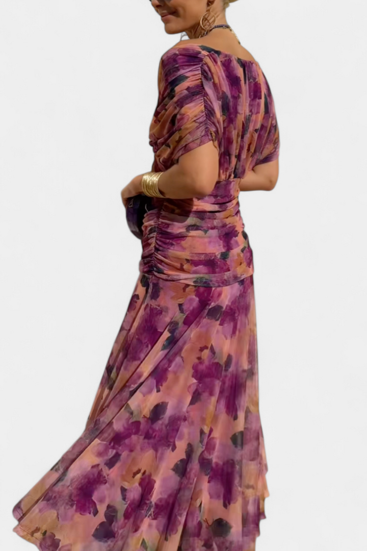 Langes, fließendes Maxikleid mit V-Ausschnitt, geraffter Taille und floralem Muster in Lila- und Rosatönen.