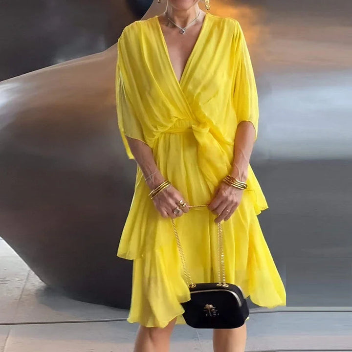 Gelbes Midikleid mit V-Ausschnitt, Wickeloptik, Taillenbindung und fließendem, gestuftem Rock.