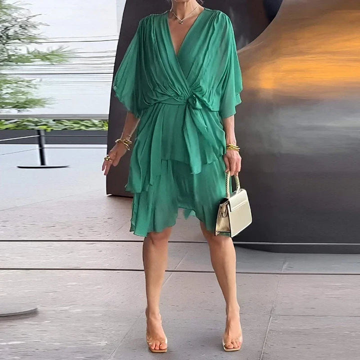 Grünes Midikleid mit V-Ausschnitt, Wickeloptik, Taillenbindung und gestuftem Rock aus fließendem Stoff.