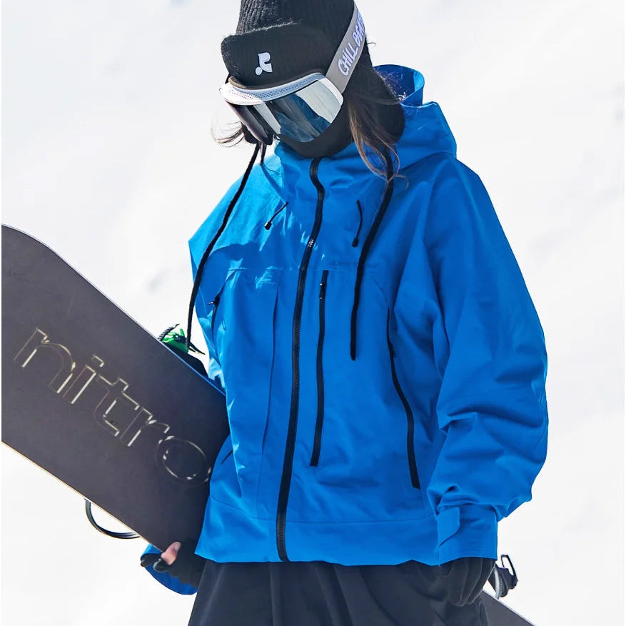 Blaue, wasserdichte Damen-Skijacke mit Kapuze und Reißverschlusstaschen, getragen beim Snowboarden im Schnee.