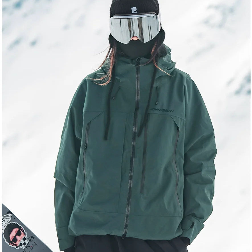 Dunkelgrüne, wasserdichte Melina Damen-Skijacke mit Kapuze und Reißverschlusstaschen in verschneiter Winterlandschaft.