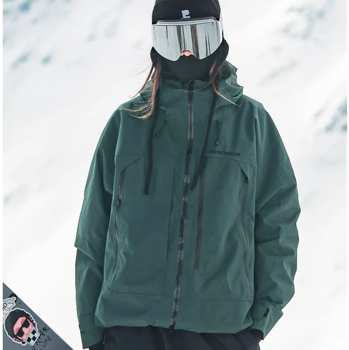 Dunkelgrüne, wasserdichte Melina Damen-Skijacke mit Kapuze und Reißverschlusstaschen in verschneiter Winterlandschaft.