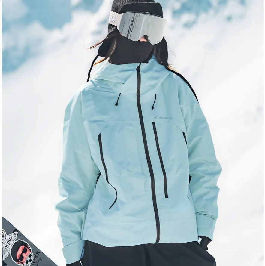 Hellblaue, wasserdichte Damen-Skijacke mit Kapuze, Reißverschlusstaschen und schwarzem Frontreißverschluss im Schnee.