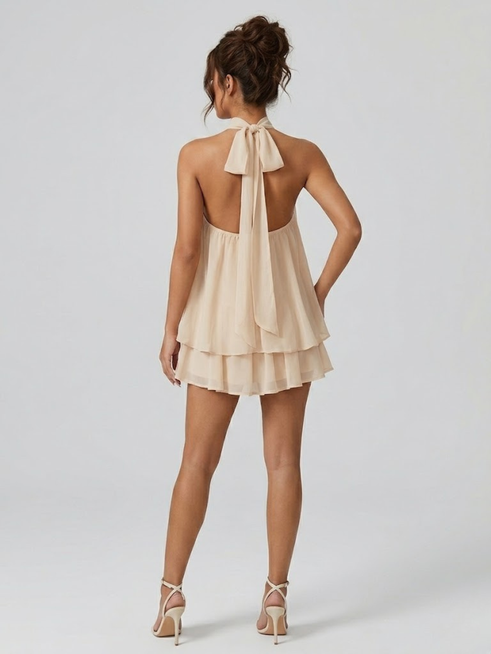 Beiges Neckholder-Minikleid mit Bindeband, offenem Rücken und fließenden Volants aus leichtem Stoff.