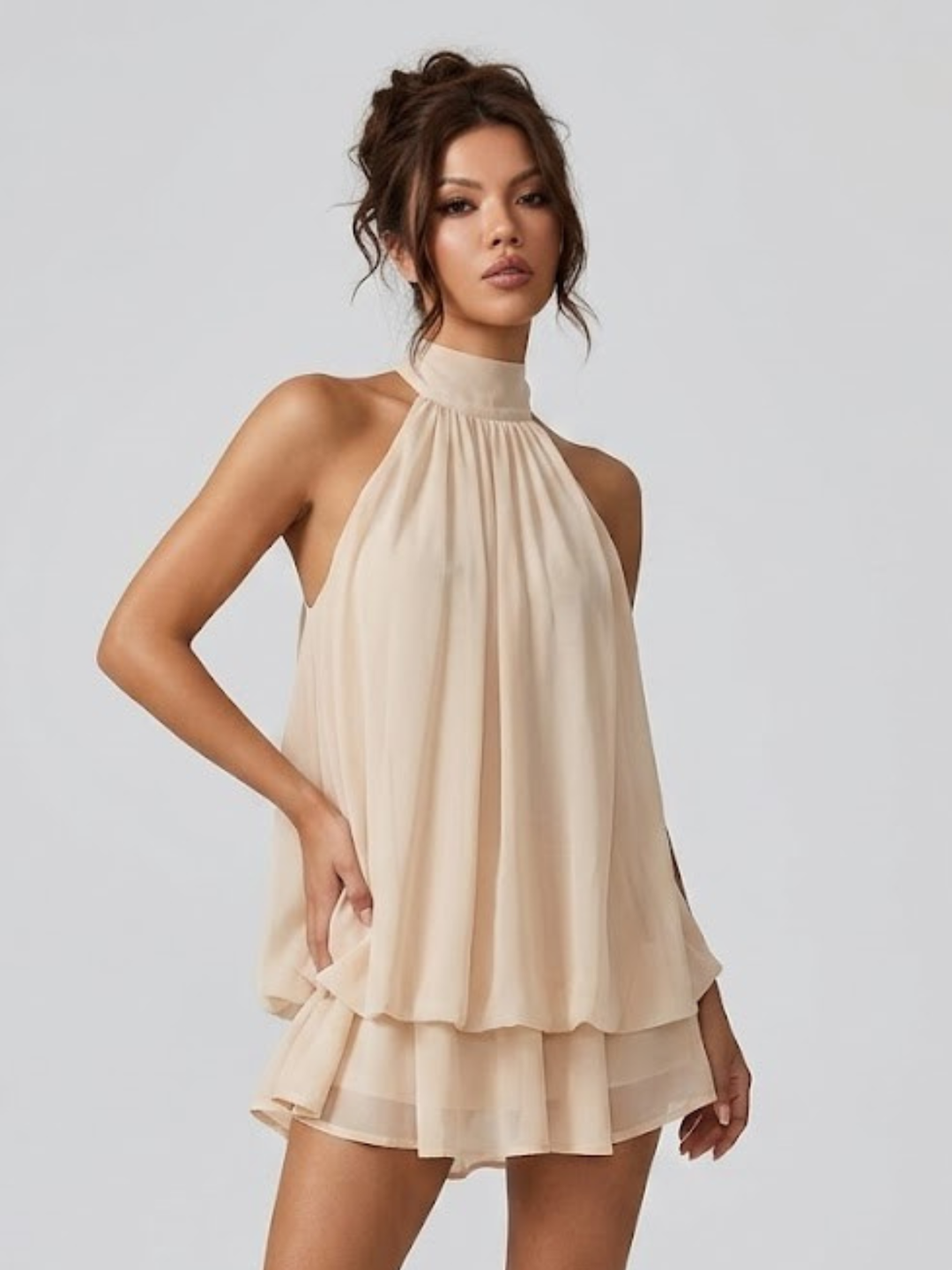 Beiges Neckholder-Minikleid mit fließendem Stoff und verspielten Volants für einen eleganten Sommer-Look.
