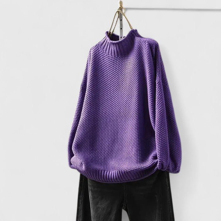 Lila Strickpullover mit Stehkragen, markantem Strukturmuster und entspannter Passform an einem Kleiderbügel.