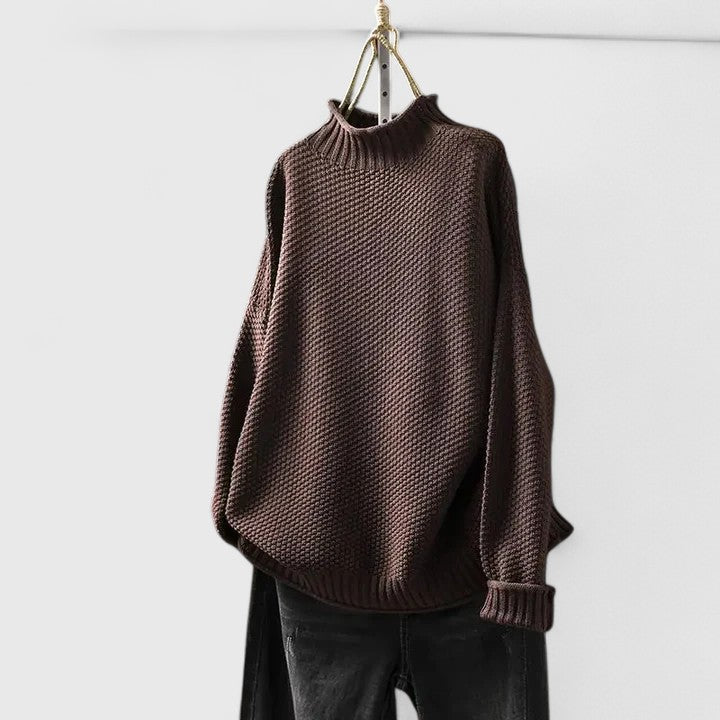 Dunkelbrauner Strickpullover mit Stehkragen, strukturiertem Muster und entspannter Passform an einem Kleiderbügel.