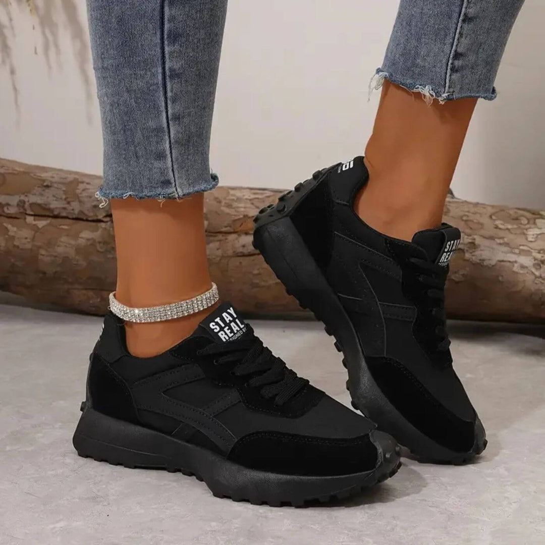 Schwarze Damen Retro-Sneaker mit Schnürung, profilierter Sohle und Stay Real Zungen-Label getragen zu Jeans.