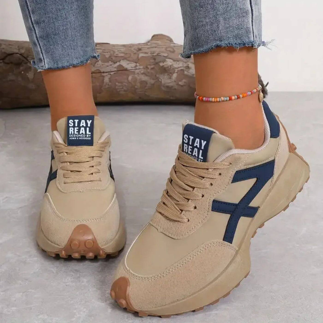 Beige Retro-Sneaker für Damen mit dunkelblauen Details, Schnürung und markanter Profilsohle im sportlichen Design.