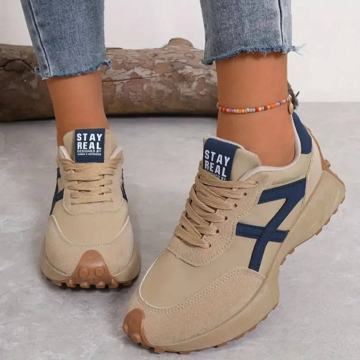 Beige Retro-Sneaker für Damen mit dunkelblauen Details, Schnürung und markanter Profilsohle im sportlichen Design.