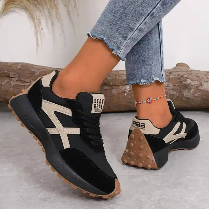 Schwarze Nina Retro-Sneaker mit beigen Kontraststreifen, Schnürung und markanter, genoppter Laufsohle in Braun.