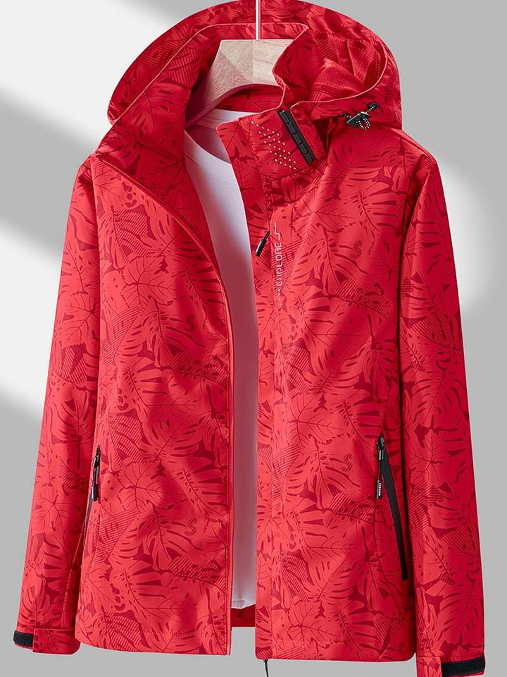 Rote wasserdichte Damenjacke mit Kapuze, Reißverschlusstaschen und auffälligem Blätter-Print für Outdoor-Aktivitäten.