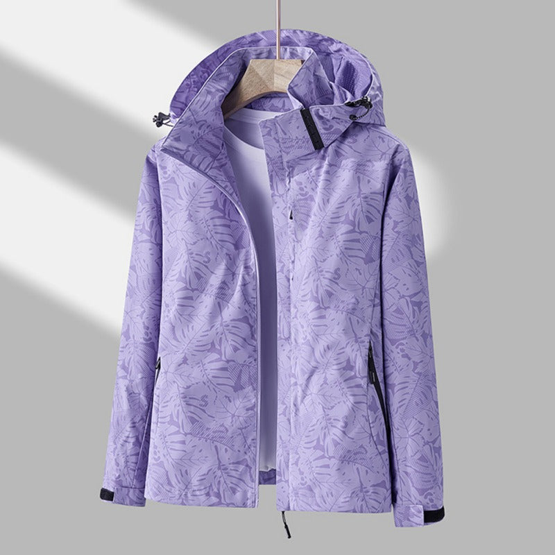 Lila Damen-Regenjacke mit Kapuze, wasserdichtem Material und auffälligem Blätter-Print sowie Reißverschlusstaschen.