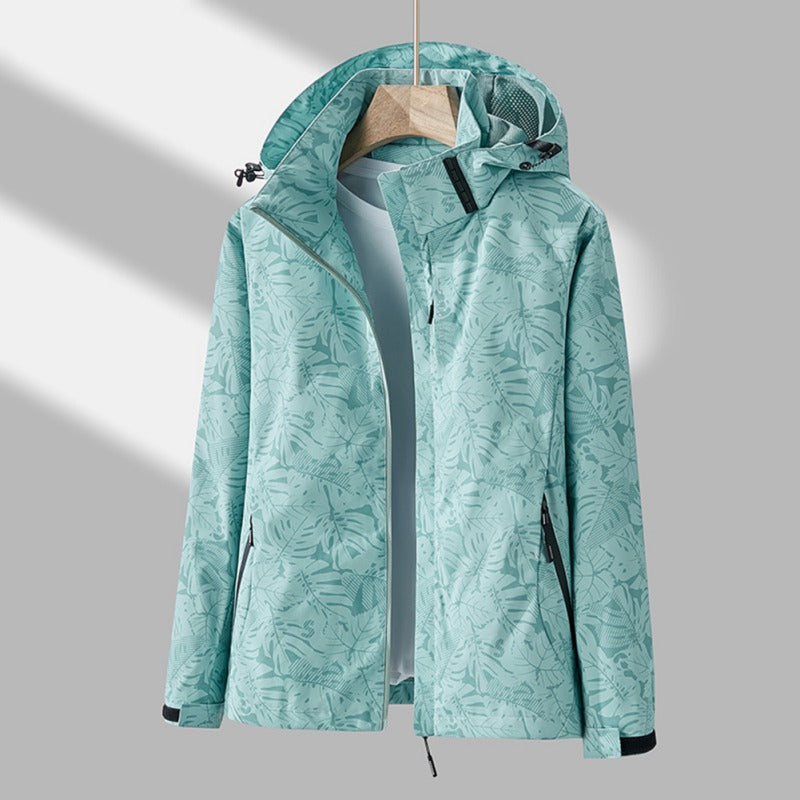 Wasserdichte Damenjacke in Mintgrün mit Blättermuster, Kapuze und Reißverschlusstaschen an einem Kleiderbügel.