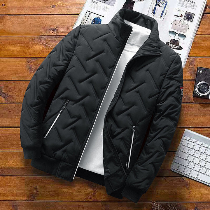 Schwarze Herren-Steppjacke mit Zickzack-Muster, Stehkragen und Reißverschlusstaschen auf einem Holztisch.