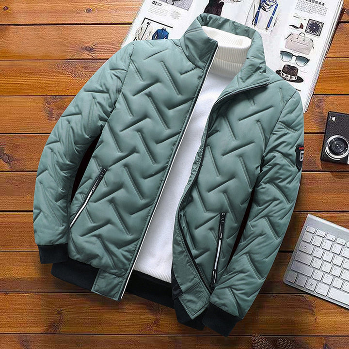 Salbeigrüne Herren-Steppjacke mit Zickzack-Muster, Stehkragen, Reißverschlusstaschen und schwarzen Bündchen.