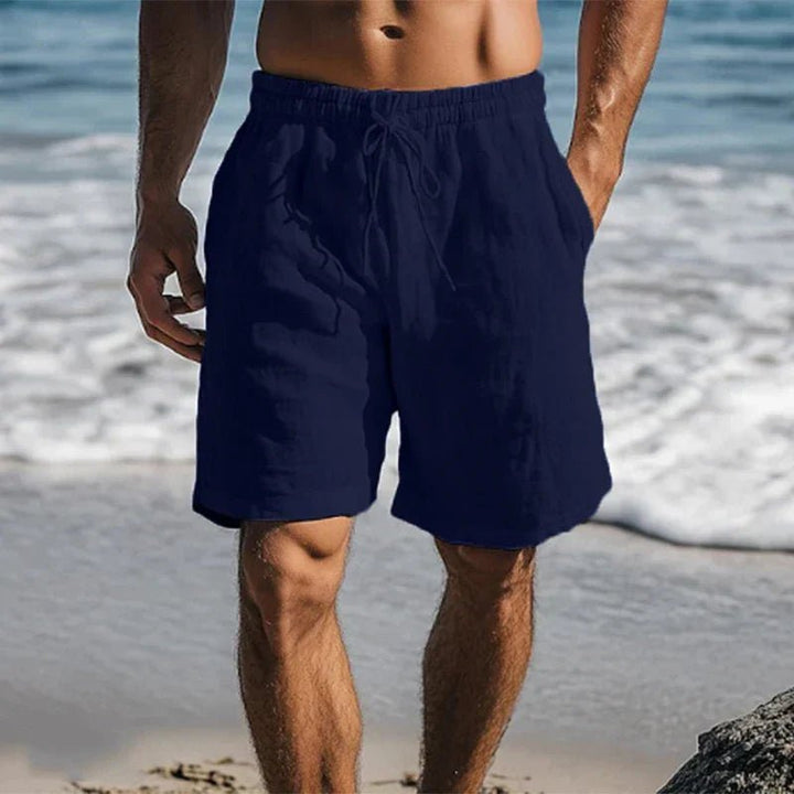 Dunkelblaue Herren-Leinenshorts mit Kordelzug und Seitentaschen in lockerer Passform am Strand.