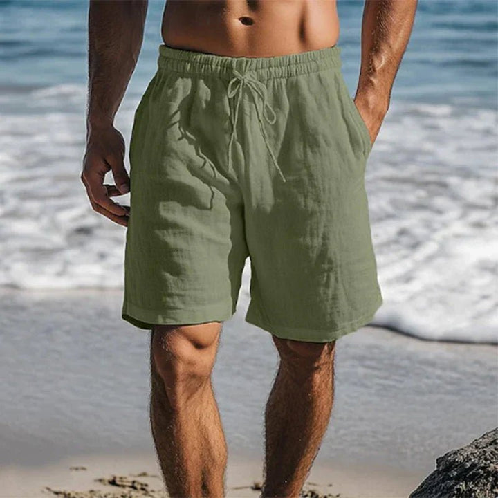 Olivgrüne Herren-Leinenshorts mit Kordelzug, Seitentaschen und lockerer Passform am Strand.