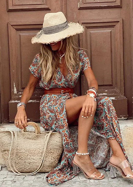 Buntes Boho-Maxikleid mit V-Ausschnitt, kurzem Ärmel und seitlichem Beinschlitz, kombiniert mit Strohhut und Basttasche.