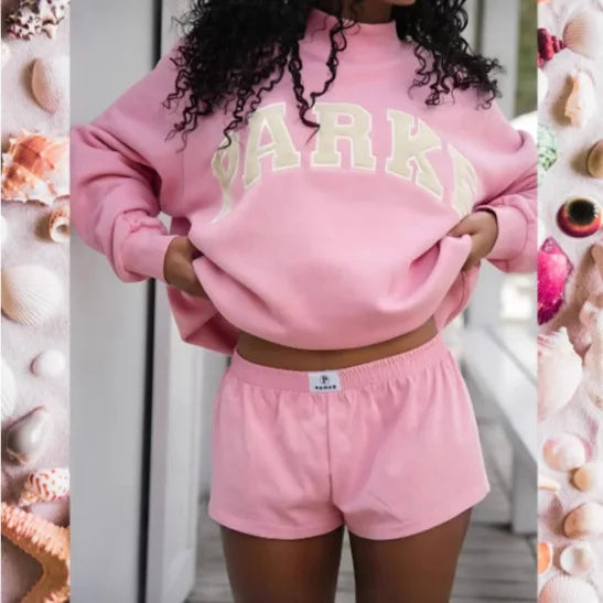 Rosa Oversized-Sweatshirt mit beigem Schriftzug-Print und passenden Shorts aus weichem Material für einen gemütlichen Look.